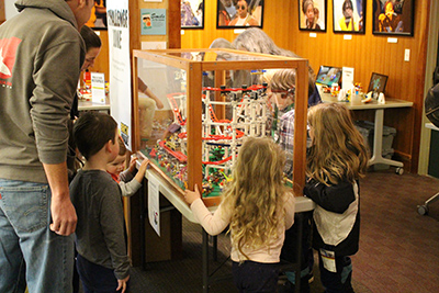 Children and adult peering into a glass case holding a Lego construction.