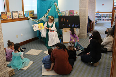 Costumed librarian reads a fairy tale to a bunch of costumed children and adults.