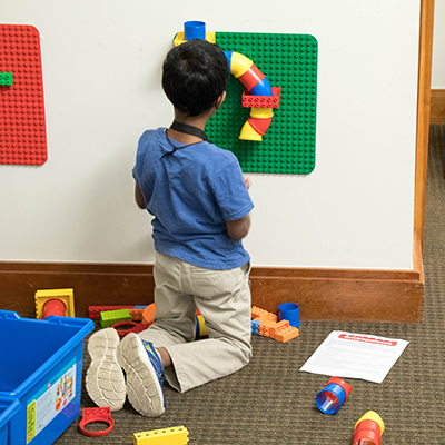 Child kneeling in front of wall mounted Lego construction.