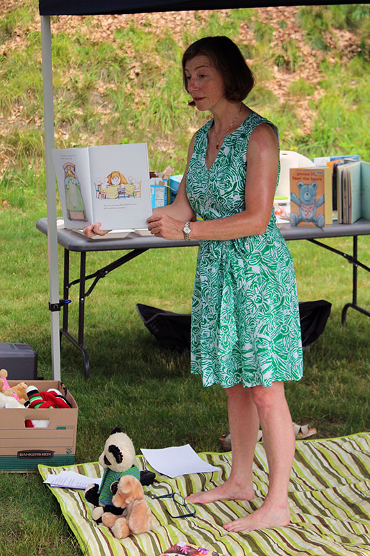 Ita displaying a book to an audience as she is standing outside on a blanket.