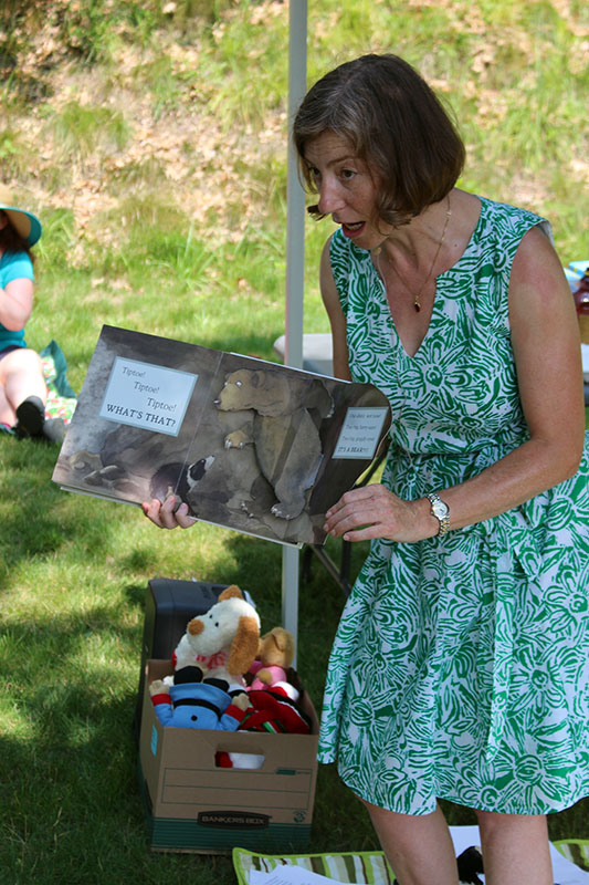 Ita standing and displaying a picture book outwards to a group outside.