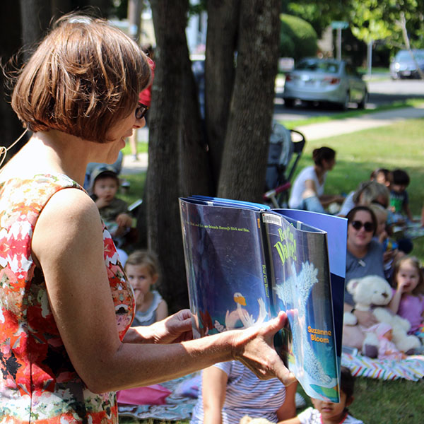 Ita standing and displaying a picture book outwards to a group outside.