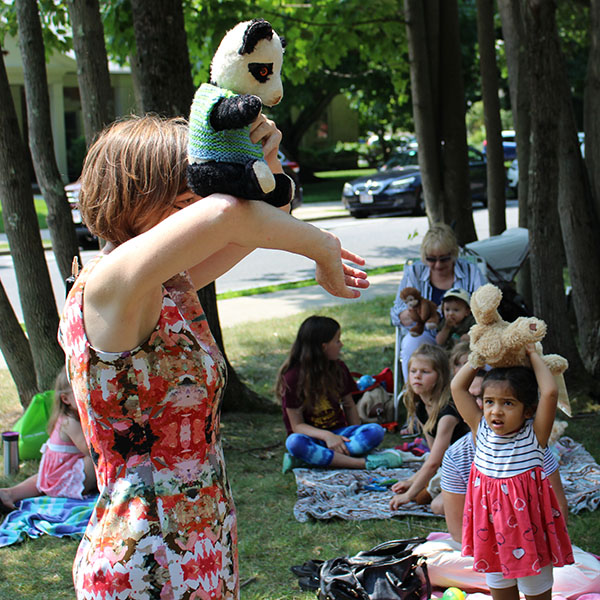 Ita is standing with a stuffed bear on her elbow raised up high near her head.