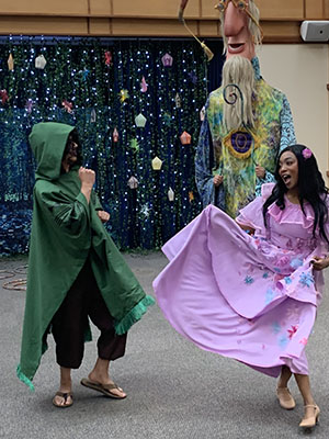 Two costumed people dance with a giant wizard towering behind them.