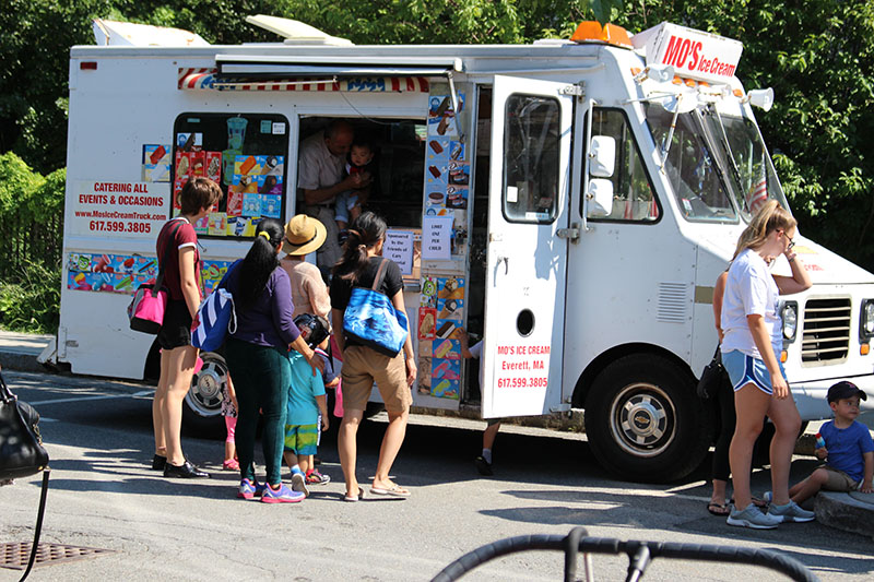 Parents and children line up outside an ice cream truck.