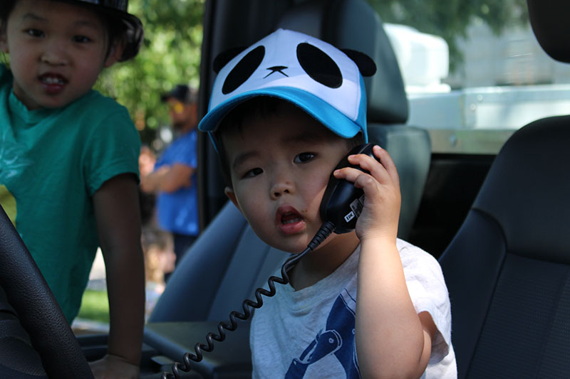Child holding up a CB radio receiver in the driver's seat of a police car.