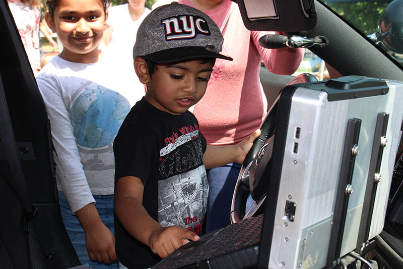 Child touching the mobile computer in the front of a police car.