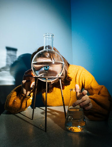 Person looking through a water beaker and has a large distorted eye.