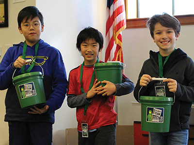 Three children holding green BRICKMANIA buckets.