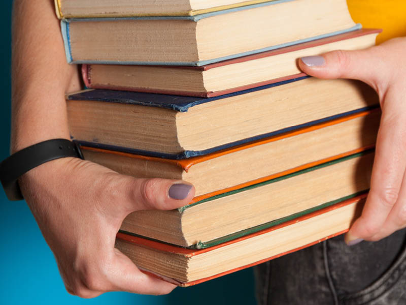 Hands carrying a pile of books