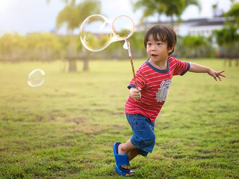 Child in a field running with a bubble wand