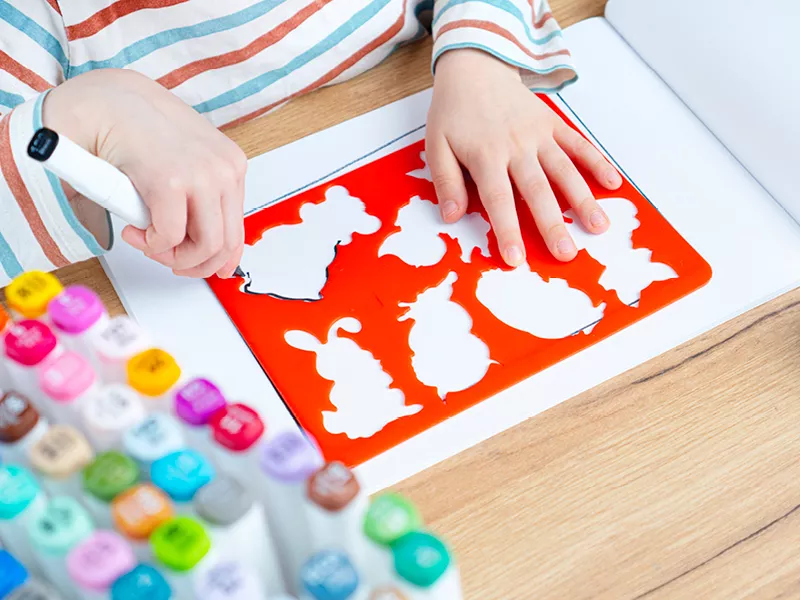Child's hands tracing animal shapes using a red plastic stencil