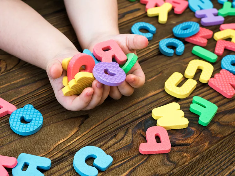 Child's hands collecting groups of colorful foam letters